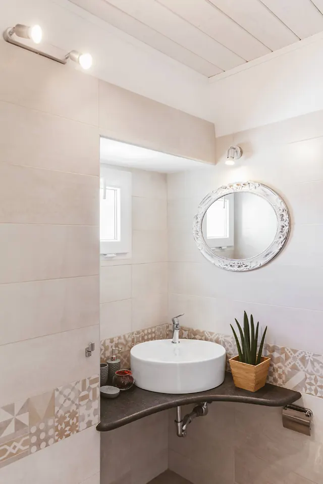 Bagno con lavabo, specchio rotondo e rivestimenti in pietra
